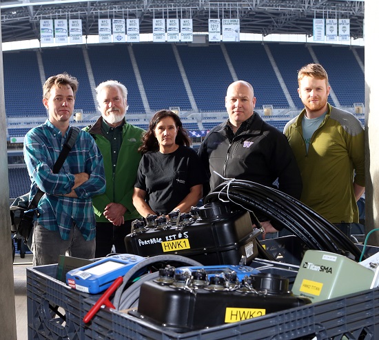Group photo of the five PNSN staff that installed the HWK stations at Century Link field in 2015, posing in Century Link field in front of the empty stands.