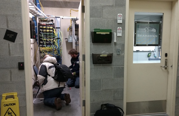 Two technicians install a seismic station in an electrical closet in Century Link Field.